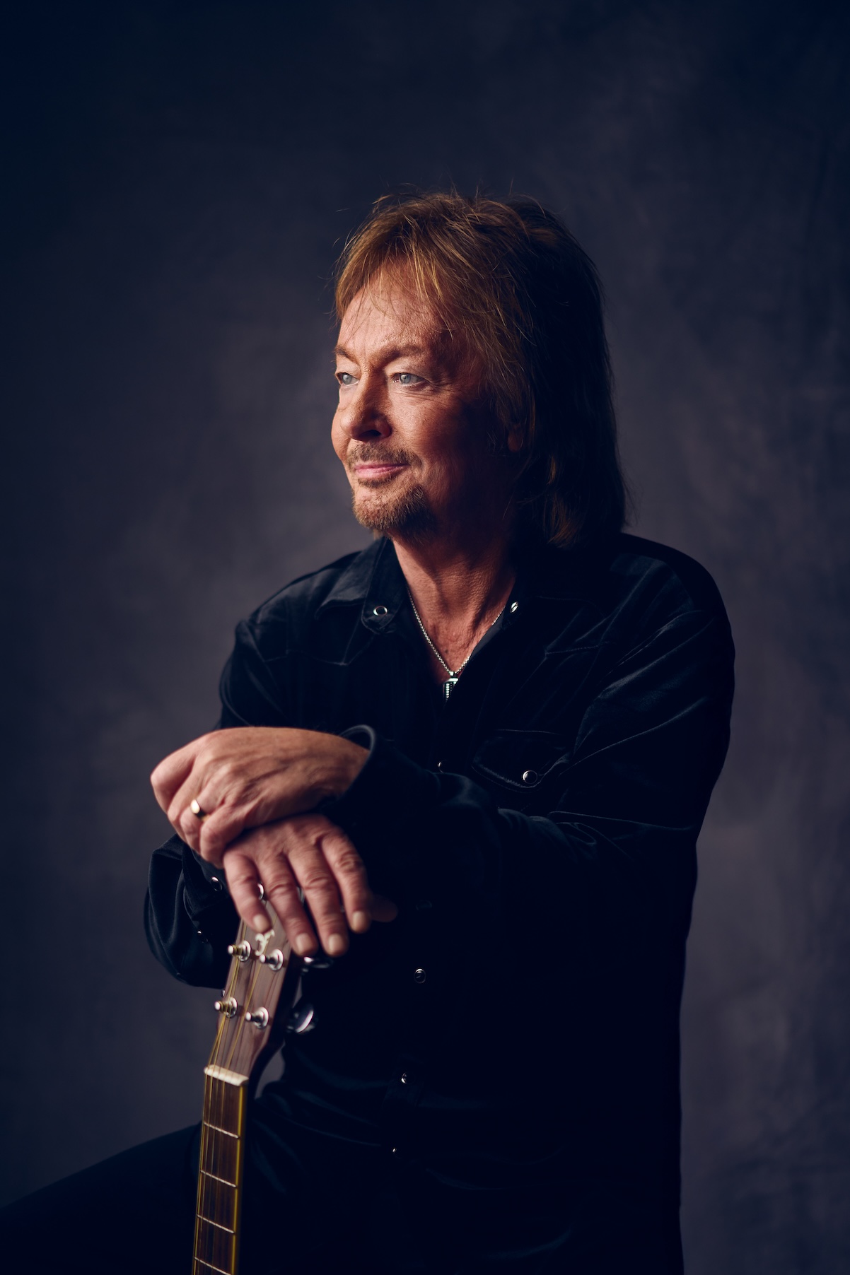 Chris Norman steht, schaut zur Seite und seine Hände ruhen auf einer stehenden Gitarre.